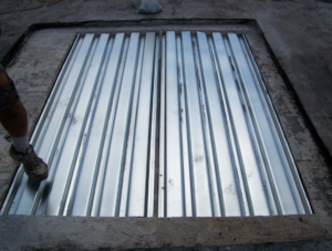 The gypsum decking was cut out within the limits of the entire framing “bay” and infilled with galvanized metal decking. The longitudinal deck panel edge was seated atop the horizontal leg of the bulb-tee section (visible in the center of the photograph) and mechanically fastened using self-tapping screws. The ends were supported by the steel purlins. The underside of the decking was prepainted to match the ceiling finish. Supplemental structural support consisting of strips of 14-gauge galvanized sheet metal were attached to the bottom of each bulb-tee section contiguous to the repair to provide additional support for the adjacent gypsum roof decking segment.