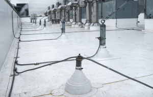 Cables interconnect the air terminals (on top of the parapet) to roof penetration (foreground) and other metal items, such as the rooftop exhaust fans and their anchorage points. Interconnections are vital to the function of the lightning protection system.